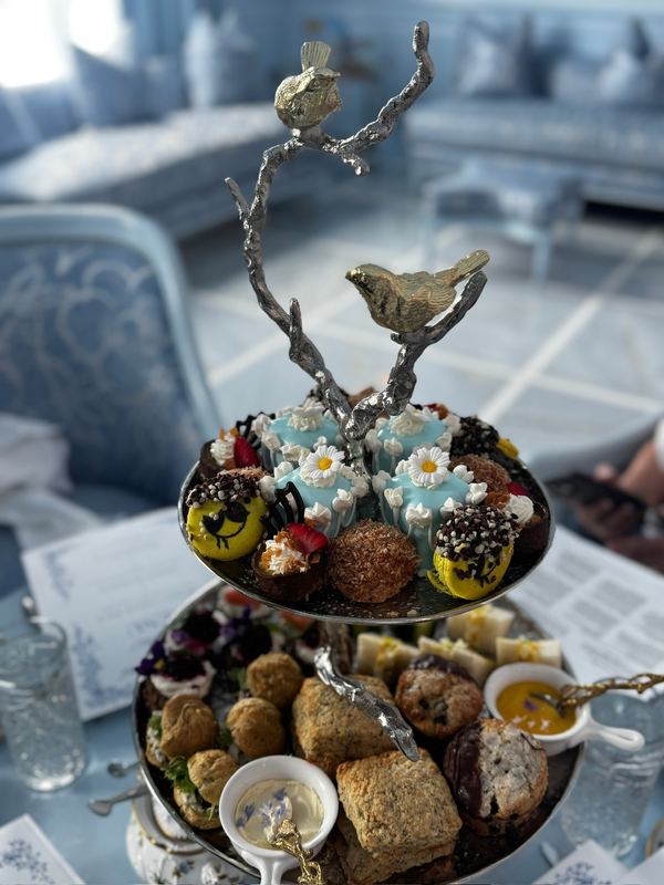 A tiered afternoon tea stand topped with a silver bird on a branch, pastries and scones below