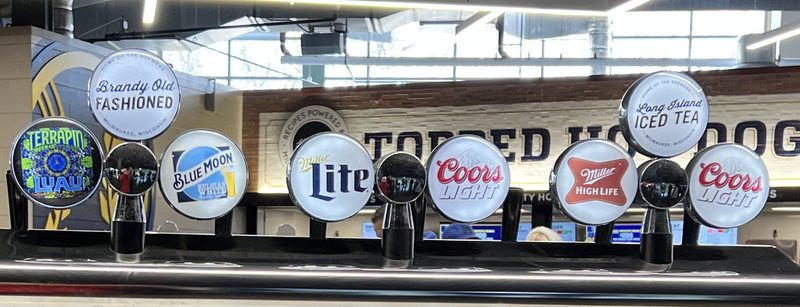 Ballpark tap handles in a row: Brandy Old Fashioned and Long Island Iced Tea beside Blue Moon, Miller Lite, Coors Light and Miller High Life