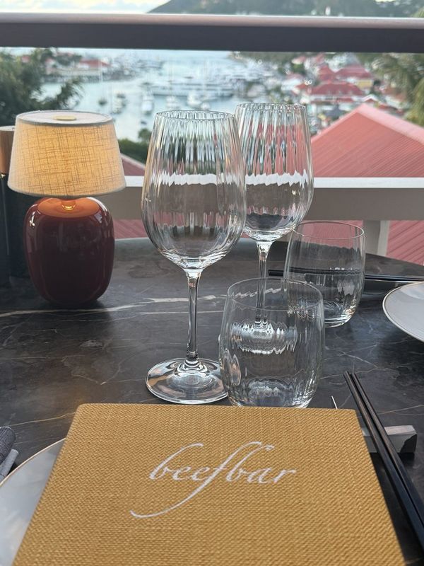 A set table at Beefbar with the menu and glasses, red roofs and the harbour beyond
