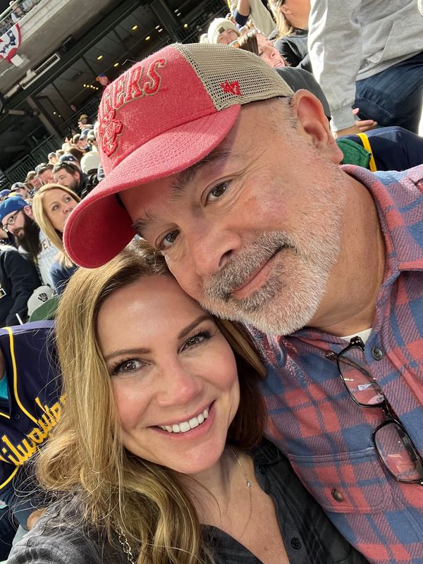 Steve and Jeannie in the stands at American Family Field, Steve in a red Rangers cap