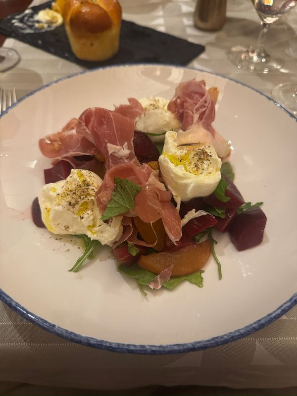 A plate of burrata with prosciutto, beets and greens