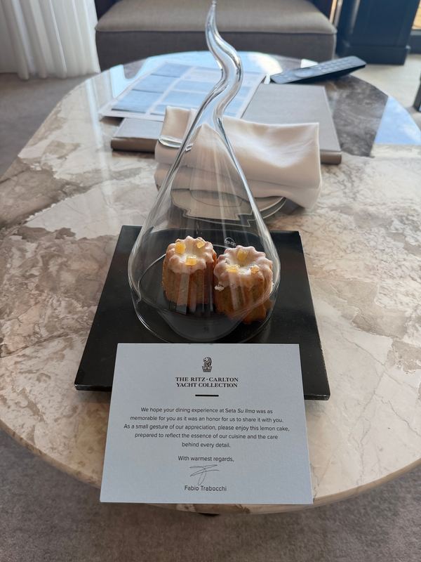 Two canelés under a glass dome on a slate, a printed note from the kitchen in front