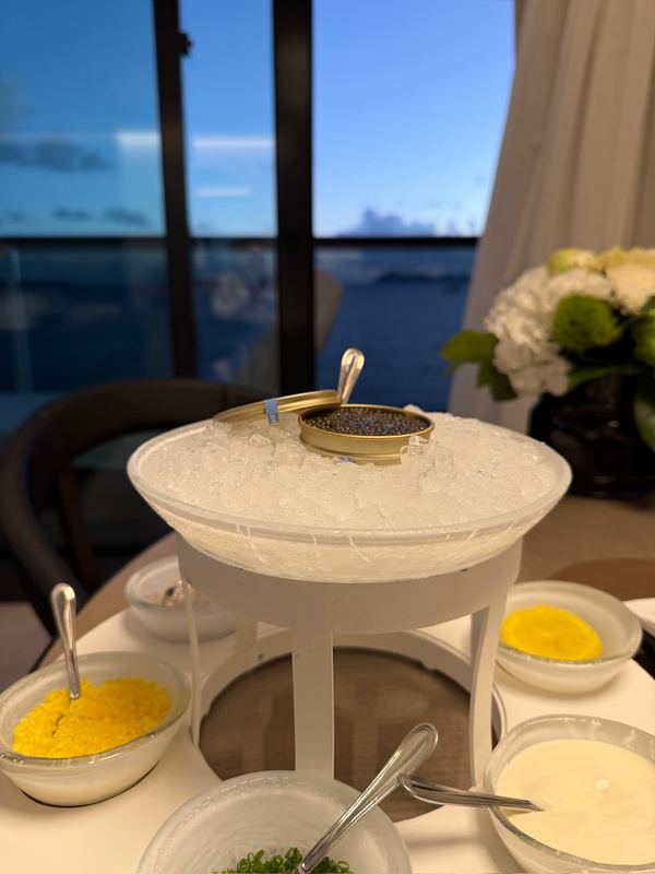 A tin of caviar on a bed of ice with bowls of egg, cream and chives, the sea in the window behind