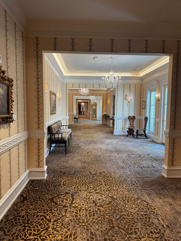 A long hotel corridor with chandeliers, wall sconces and an ornate patterned carpet