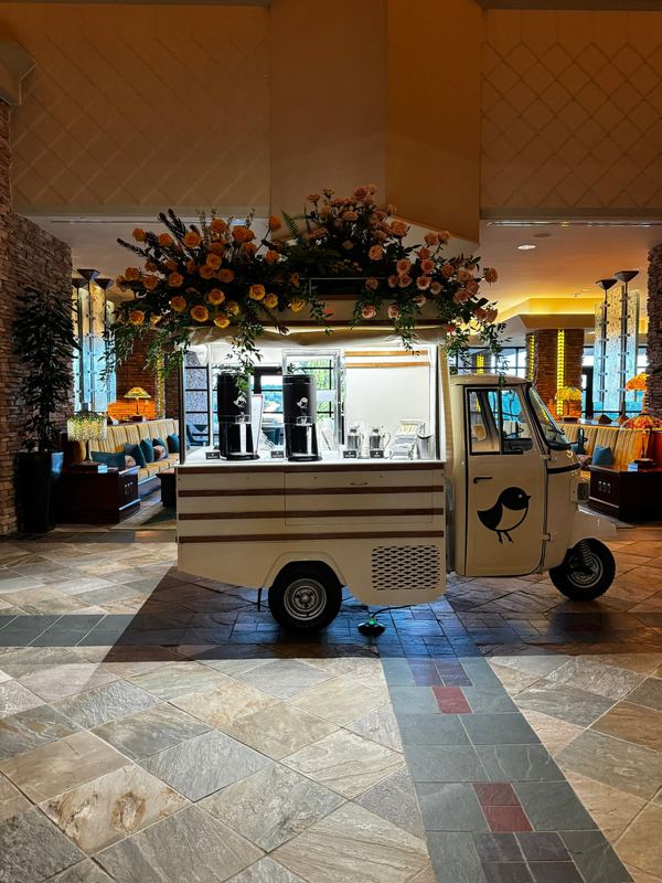 A vintage three-wheeler coffee cart under a hanging arrangement of flowers in the lobby at Falling Rock