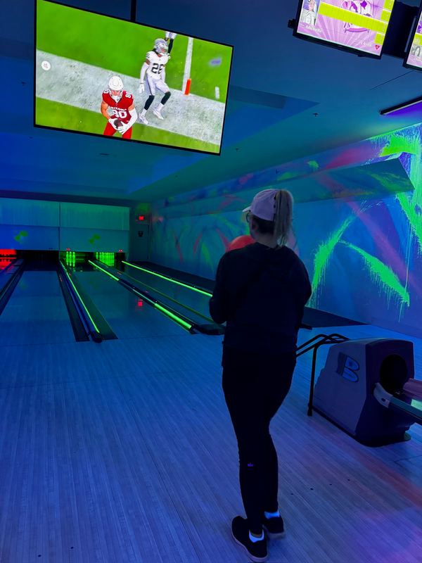 A bowler at a lane under blacklight, screens above showing football