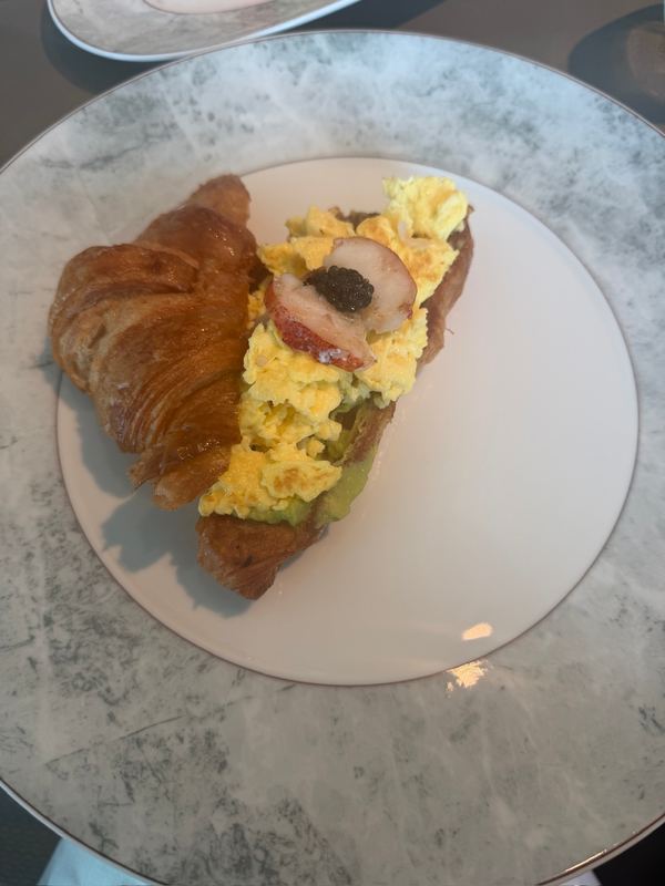 A croissant topped with scrambled eggs, lobster and caviar on a marbled plate