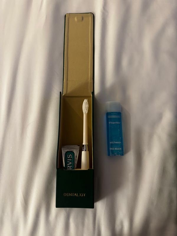 An open green dental kit box on the bed with a toothbrush, toothpaste and mouthwash