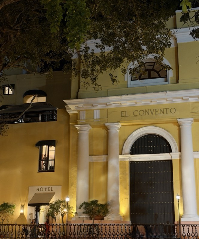 The lamplit yellow facade and arched door of El Convento at night, Old San Juan
