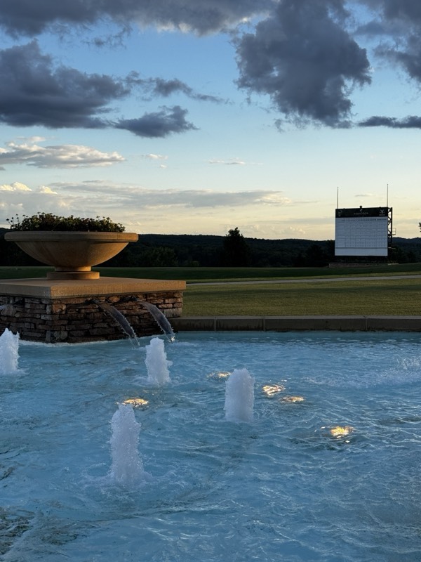 Lit fountain jets in a pool beside a fairway at dusk