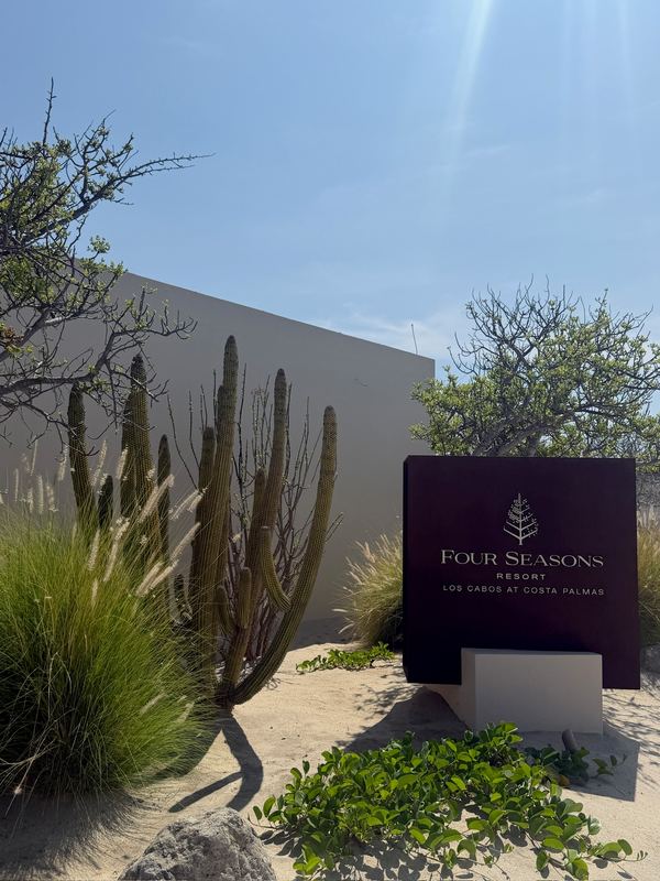 The resort sign at the entrance, cactus and grasses in front.