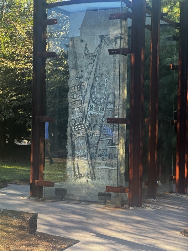 A graffitied segment of the Berlin Wall held in rusted steel posts among trees in the grounds at Nemacolin