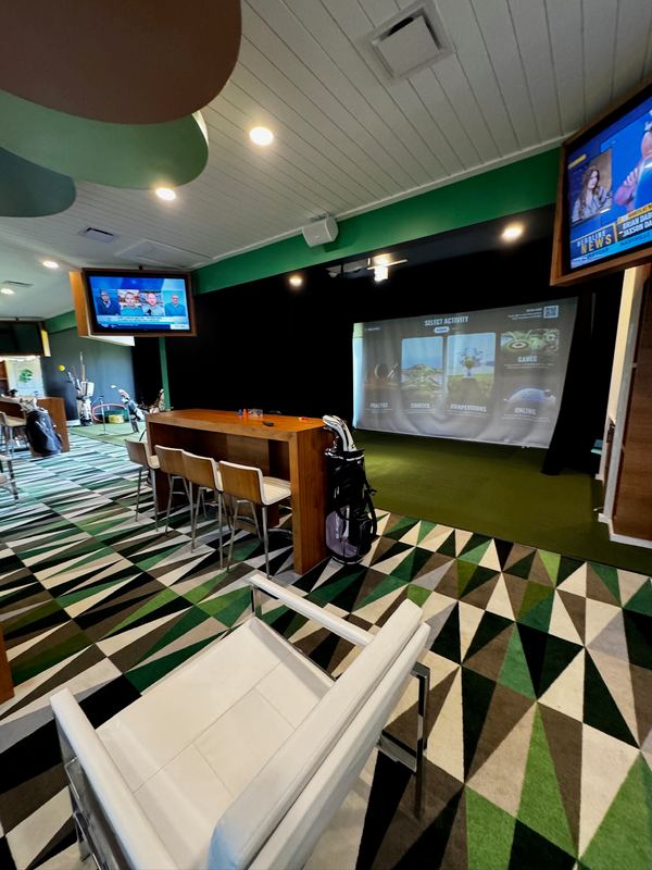 Golf simulator bays with screens, a bar counter and a geometric carpet
