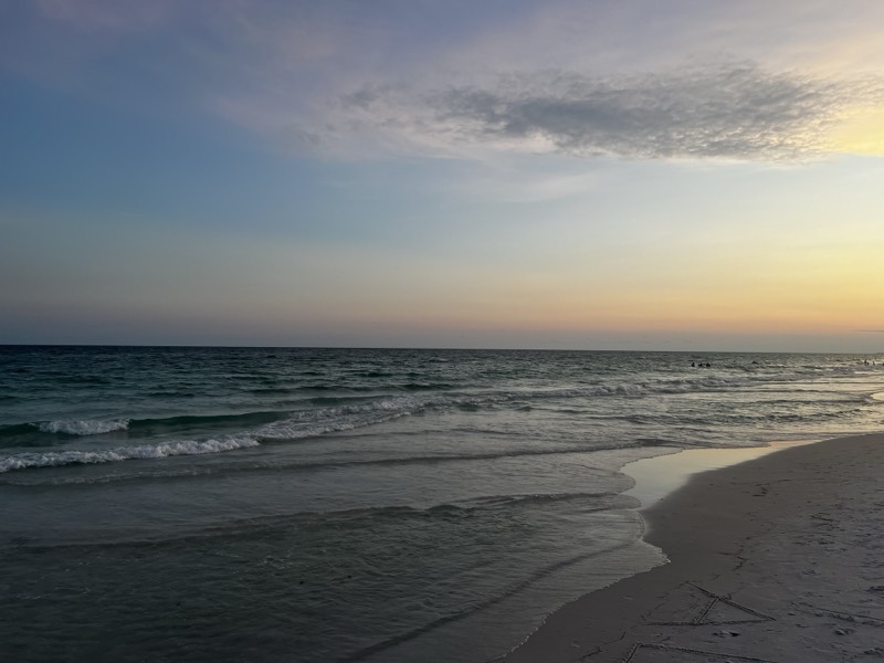 Low shorebreak curling on wet sand under a pale dusk sky