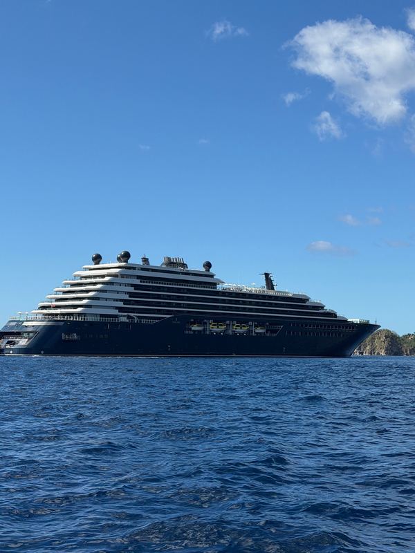 Ilma, dark-hulled with white upper decks, at anchor on a blue sea under a blue sky