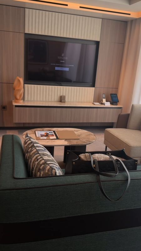 The Grand Suite living room, sofa and armchair around a marble table, the screen on the wall showing a welcome by name