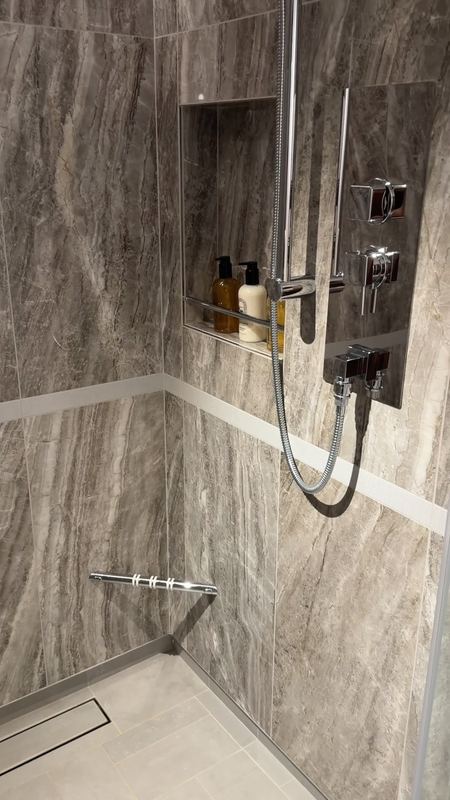 A walk-in shower in marble in the Grand Suite bathroom, rain head and hand shower with the amenities in a niche