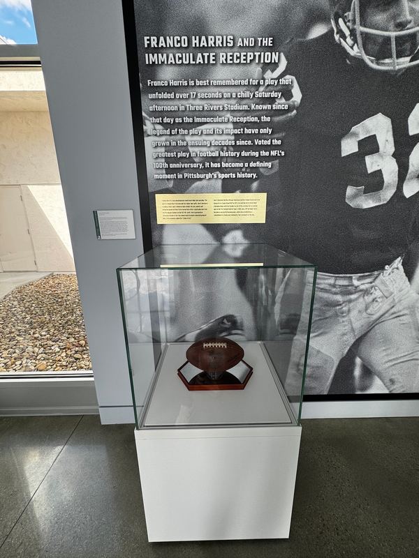 The Immaculate Reception football in a glass case in front of a wall panel about Franco Harris