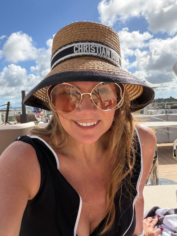 Jeannie smiling on deck in a straw hat and sunglasses