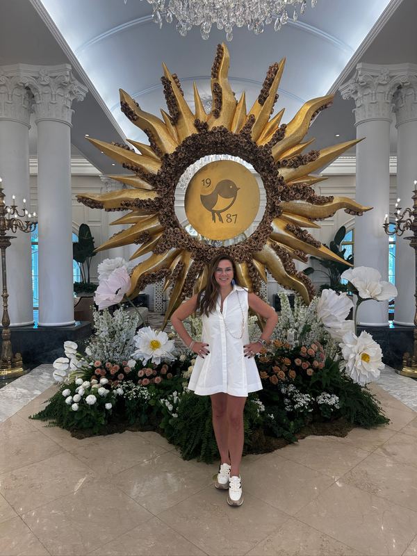 Jeannie in a white dress in front of a gilded sun sculpture in the lobby, the resort's bird and the year 1987 at its centre