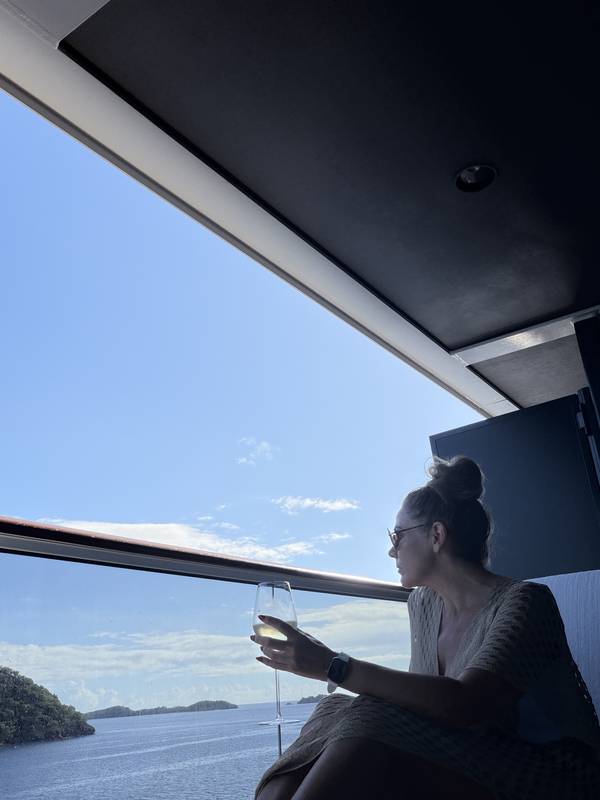 Jeannie with a glass of wine at the panoramic window of the suite, the sea and islands below