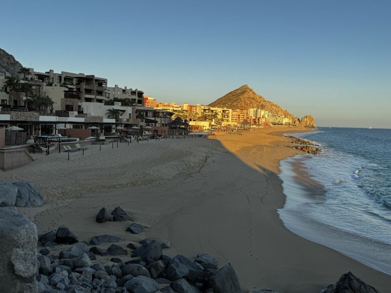 Curved beach and hillside town glowing gold below the headland rock, Land’s End, Cabo San Lucas