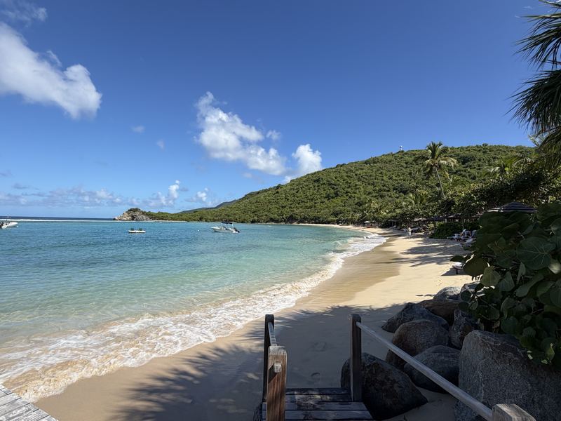 Crescent white-sand bay against a green hillside with wooden steps in the foreground, Virgin Gorda