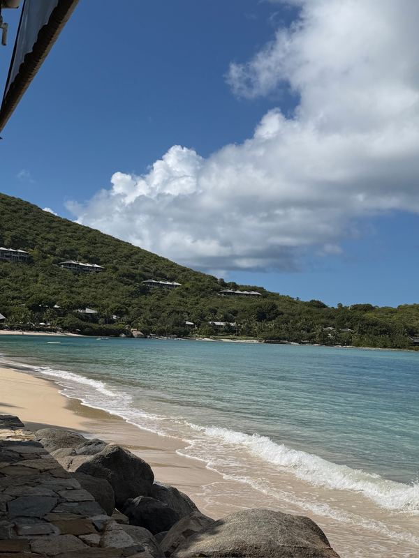 Little Dix Bay from the rocks at the end of the beach, clouds over the green hill