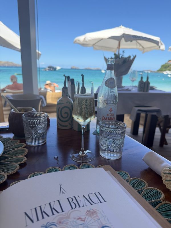 A table set under a white umbrella at Nikki Beach with the turquoise bay behind