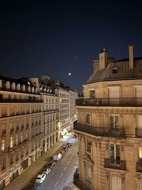 A Paris street at night from the hotel window, a crescent moon over the rooftops