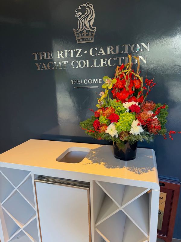 The Ritz-Carlton Yacht Collection crest on a dark wall above a vase of red and white flowers
