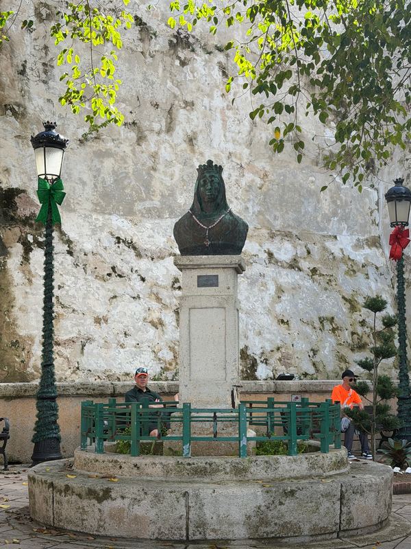 A bronze figure with a rosary at its neck, against the old city wall