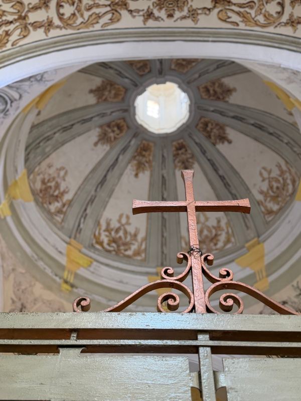 An iron cross on a gate below a painted chapel dome