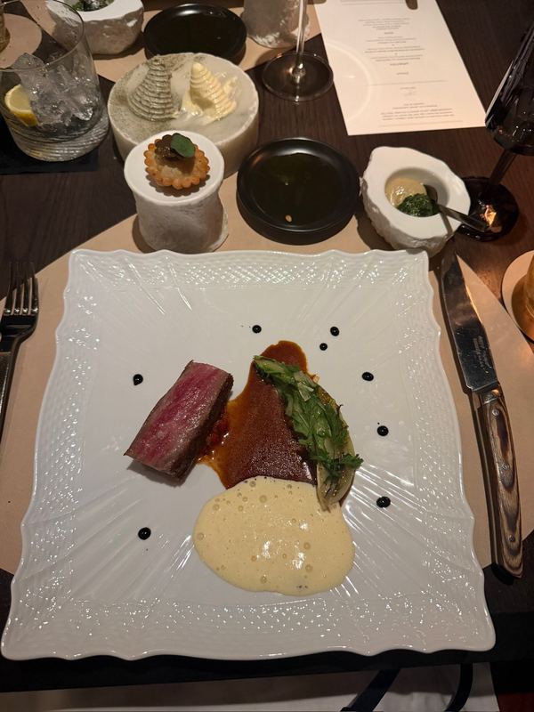 A beef course at Seta su Ilma, the sauces dotted on an embossed white plate, the menu card beyond