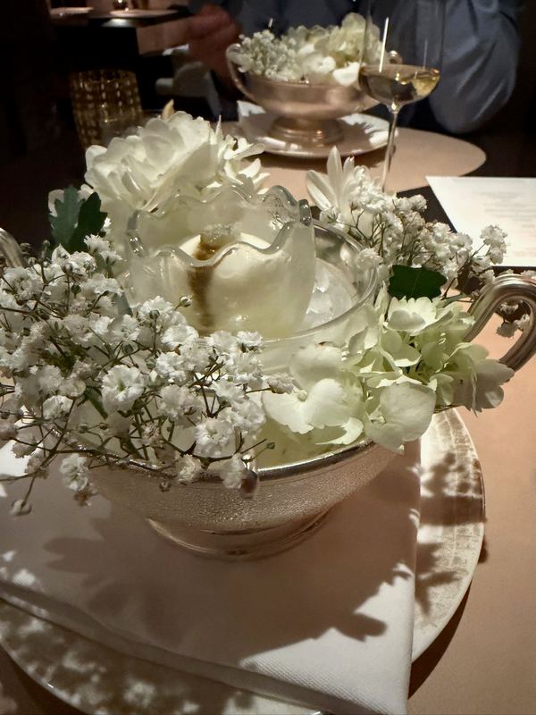 The table at Seta su Ilma: white flowers in a silver tureen, wine glasses and the menu behind