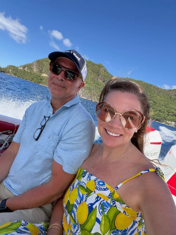 Steve and Jeannie in sunglasses on a speedboat, the wake and green hills behind