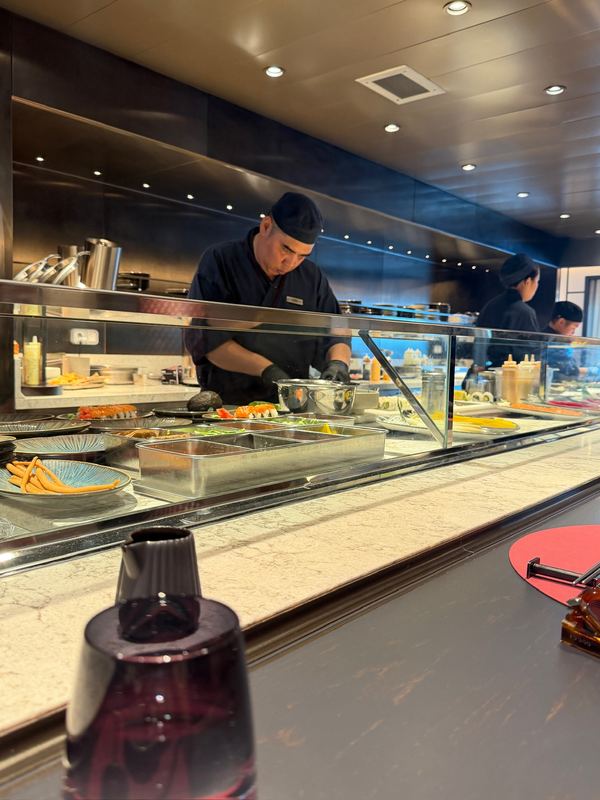Two chefs in black at work behind the glass counter at Memori, the sushi bar on board