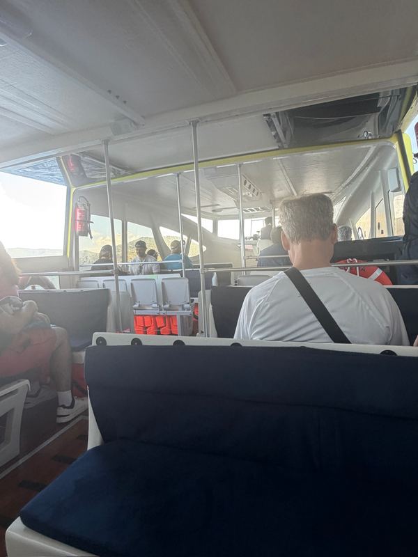 Inside the ship's tender on the way in, passengers in the seats ahead and the island through the windows