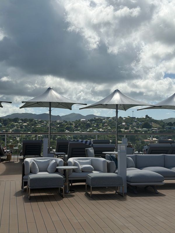Grey loungers under white umbrellas on the top deck, the hills of St. John's, Antigua, behind