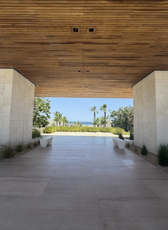 Travertine breezeway with a wood-slat ceiling framing palms and the sea