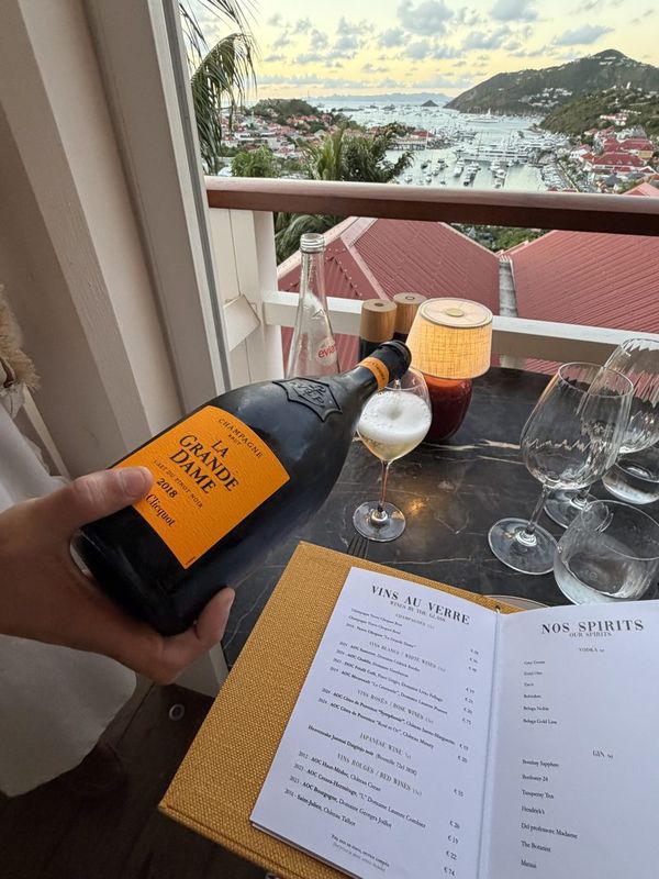 A bottle of Veuve Clicquot being poured beside a wine list, harbour view behind
