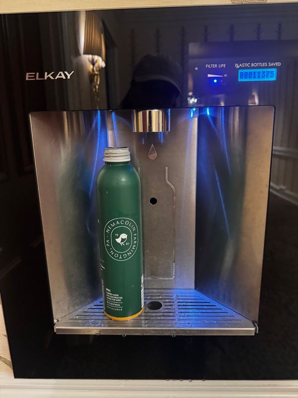 An Elkay refill station filling a green aluminium Nemacolin water bottle