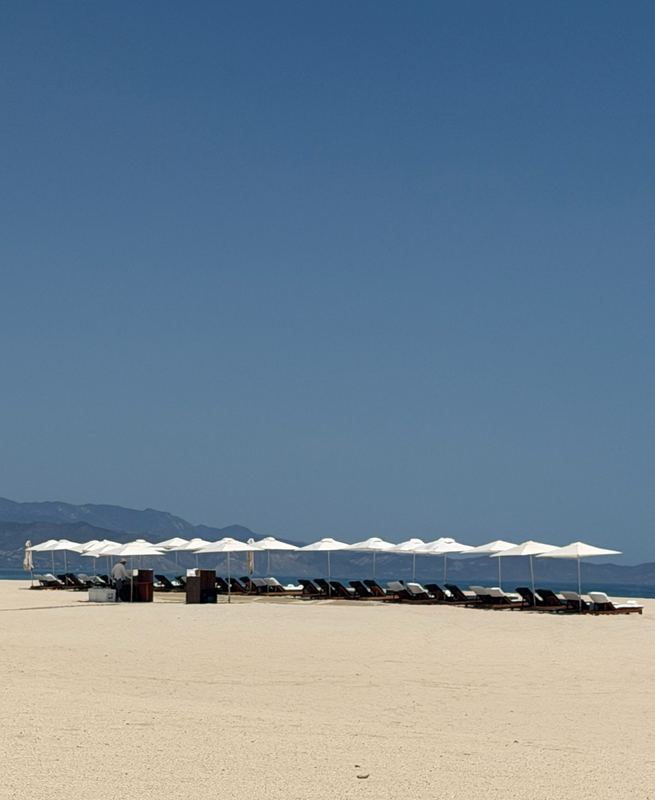 The line of white umbrellas on the resort beach, mountains across the water.