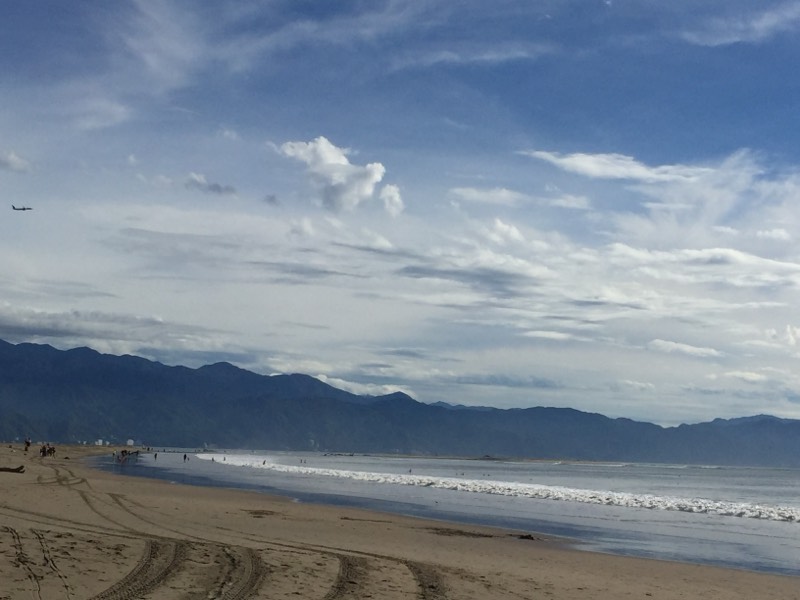 Wide tide-marked beach under a mountain range and layered cloud, distant figures on the sand